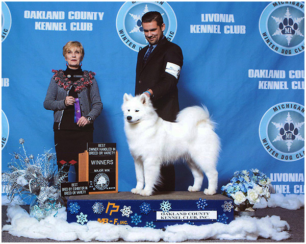 A woman and man standing next to a white dog.