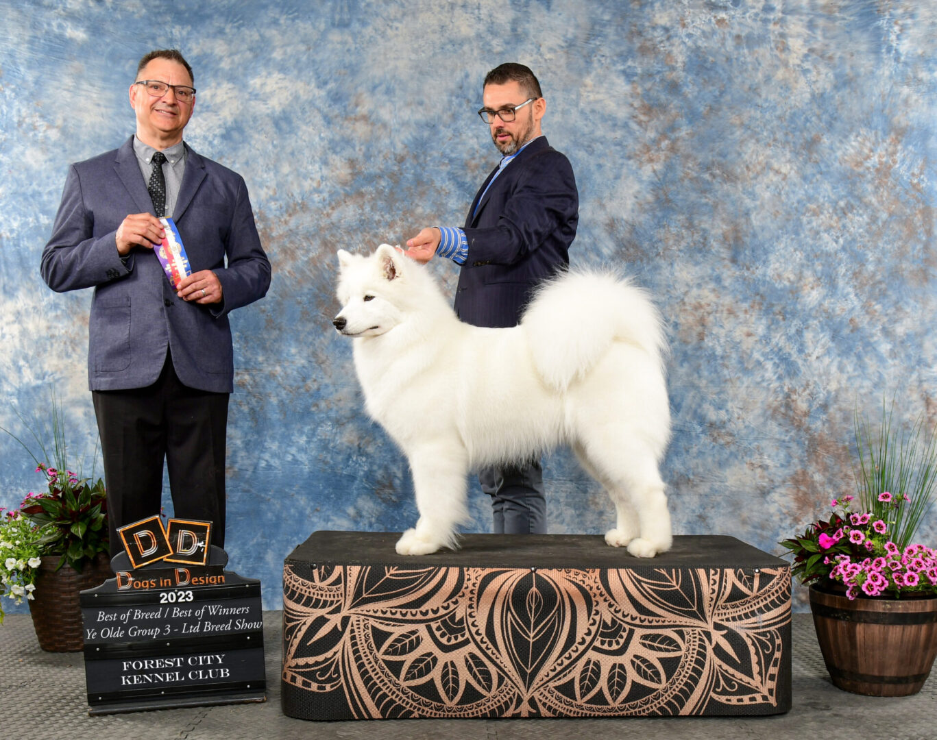 Two men standing next to a white dog on top of a podium.